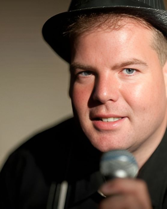 David Spatola singing into a microphone, wearing a black fedora and jacket
